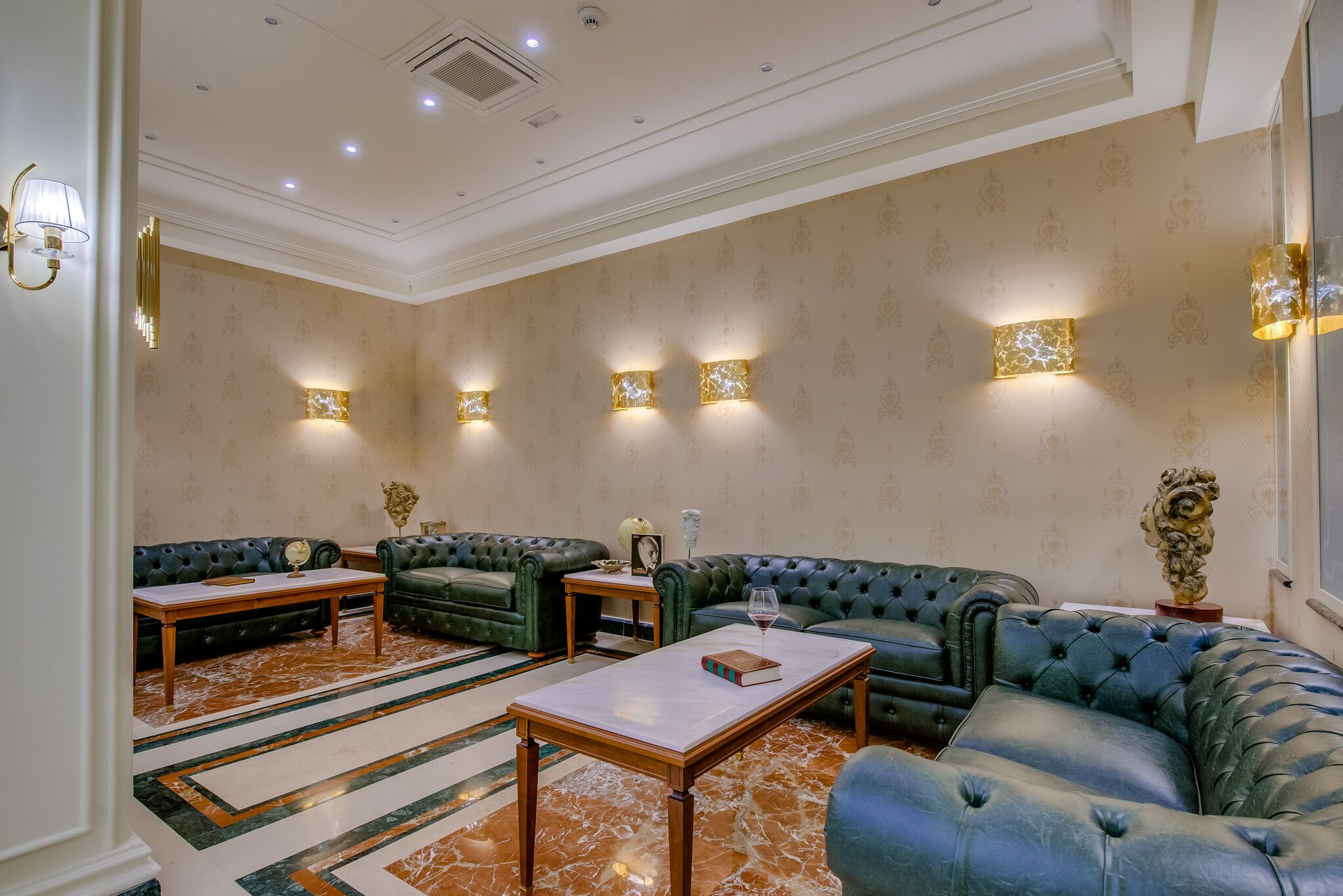 Una sala de estar lujosa con un sofá verde, piso de mármol y apliques de pared.