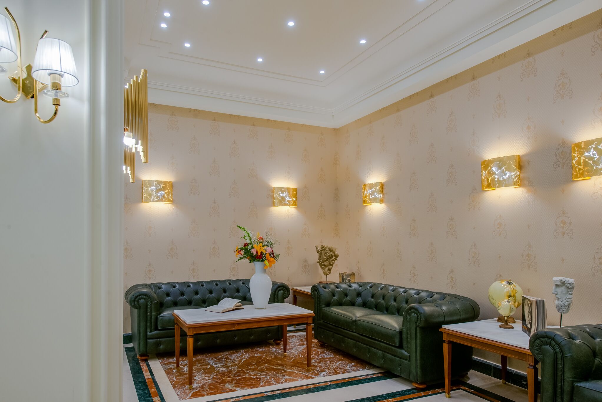 Una habitación con un sofá de cuero verde, un jarrón blanco con flores y una alfombra con diseño de mármol.