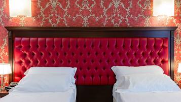 Una habitación de hotel con cabecera tapizada roja, dos camas blancas y papel tapiz decorativo.