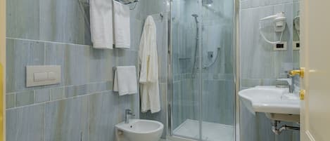 Un baño moderno con inodoro, bidé, cabina de ducha de vidrio y lavamanos.