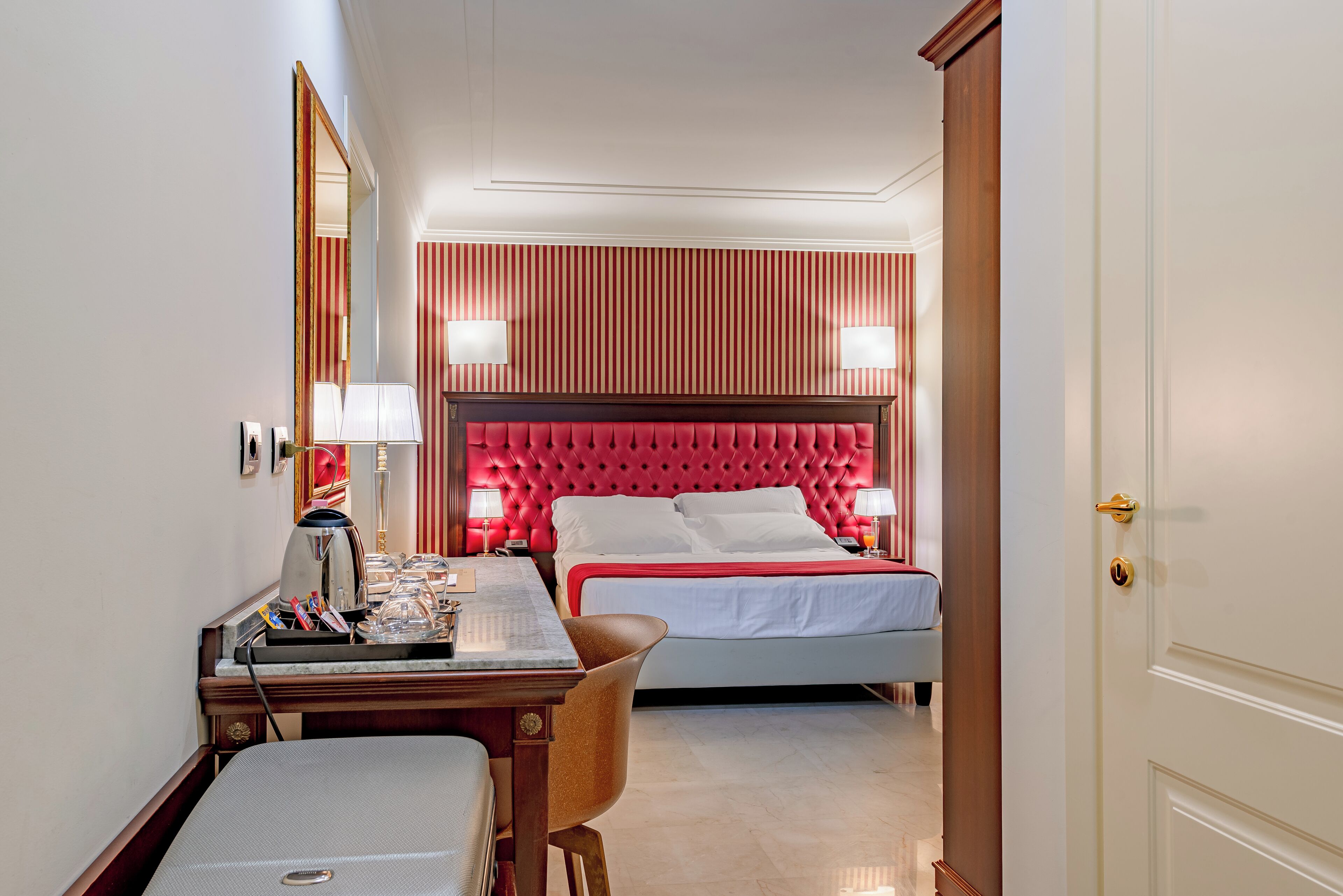 Una camera d'albergo con un letto, una scrivania, una sedia, uno specchio e una porta.