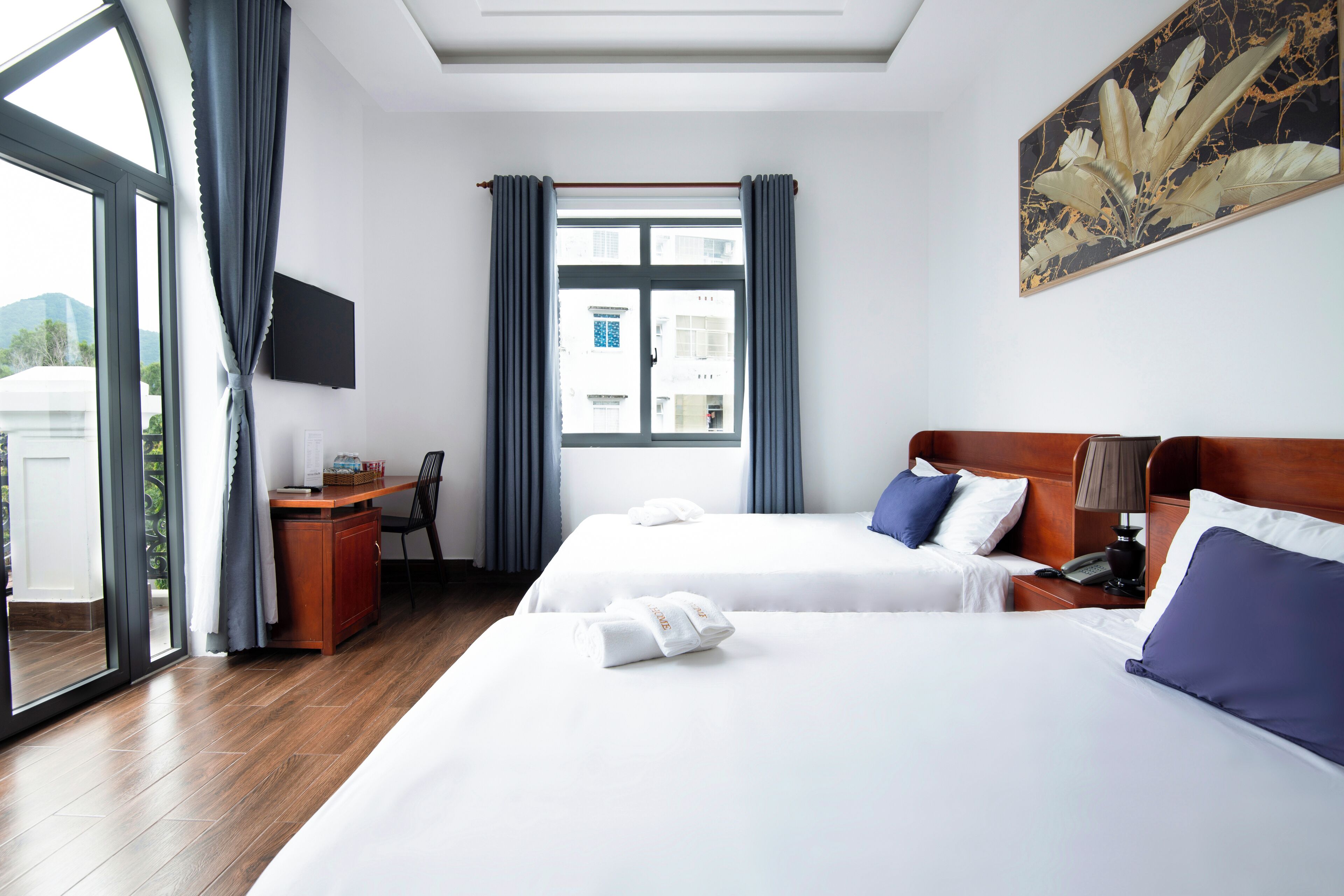 A hotel room with two beds, a desk, a chair, a TV, and a window with curtains.