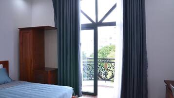 A bedroom with a bed, a wooden wardrobe, and a balcony with a view of greenery.