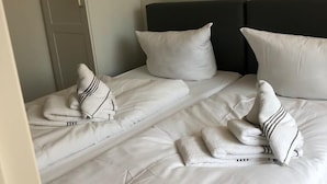 A neatly made bed with white linens and striped pillows, a dark headboard, and a closed wardrobe. - Sylter Leuchtfeuer (Sylt)