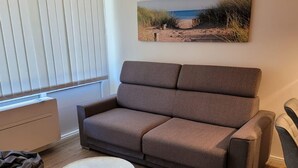 A modern living room with a brown sofa, a round coffee table, and a painting of a beach scene on the wall. - Sylter Leuchtfeuer (Sylt)