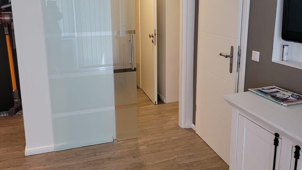 A hallway with wooden flooring, white doors, and a white cabinet with black handles. - Sylter Leuchtfeuer (Sylt)
