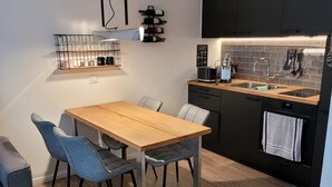 A modern kitchen with a wooden dining table and chairs, a black countertop, and a built-in oven. - Sylter Leuchtfeuer (Sylt)
