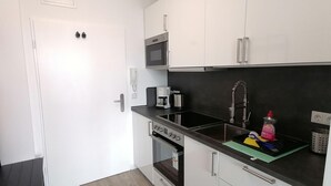 A compact kitchen with white cabinets, a microwave, a coffee maker, and a stainless steel sink. - App. Friesenkoje (Sylt)