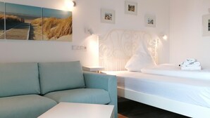 A hotel room with a bed, a sofa, a bedside table, and a wall with framed pictures. - App. Friesenkoje (Sylt)