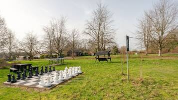 An outdoor chess set on a grassy field with benches and a picnic table in the background.