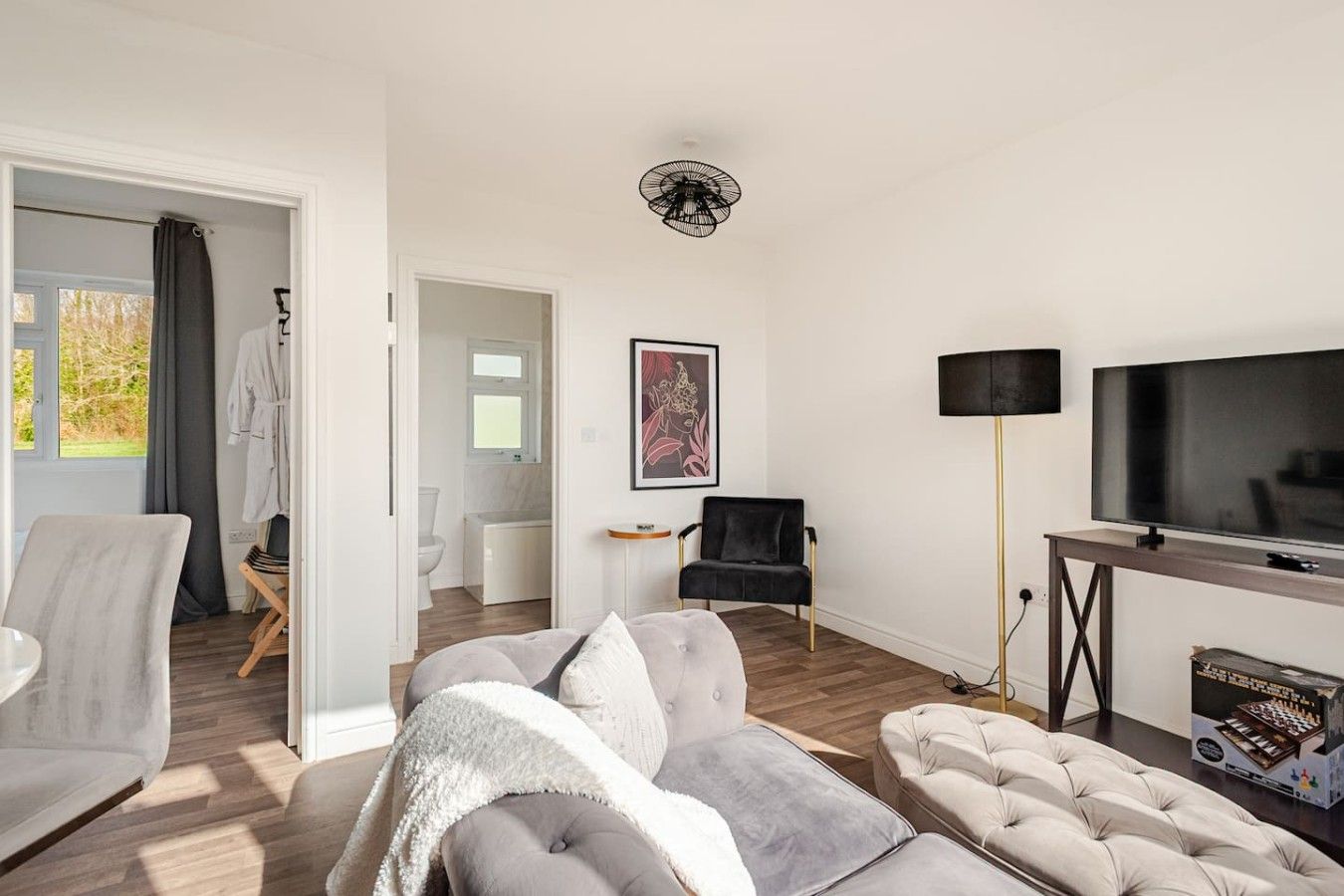 Un salon moderne comprenant un canapé, un fauteuil et un pouf, un téléviseur à écran plat et une lampe sur pied.