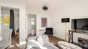 Un salon moderne comprenant un canapé, un fauteuil et un pouf, un téléviseur à écran plat et une lampe sur pied.