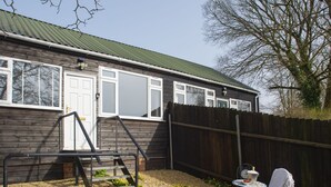 Ein Whirlpool in einem Garten mit einem Holzhaus, einem Holzzaun und einem Tisch mit einem Stuhl.