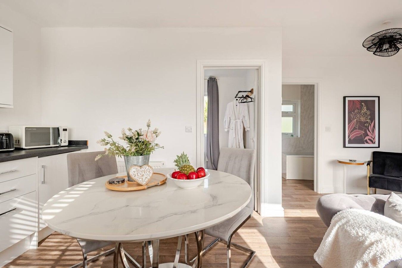 Une cuisine moderne avec un plan de travail blanc, un four à micro-ondes et un coin repas doté d’une table en marbre.
