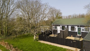 Ein zweistöckiges Haus mit grüner Dachdeckung, einem umzäunten Garten und einem Baum im Vordergrund.