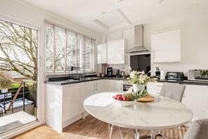 A modern kitchen with white cabinetry, a marble countertop, and a dining area with a white table and chairs. - Secluded Hut with a Private Hot Tub (Blandford Forum)