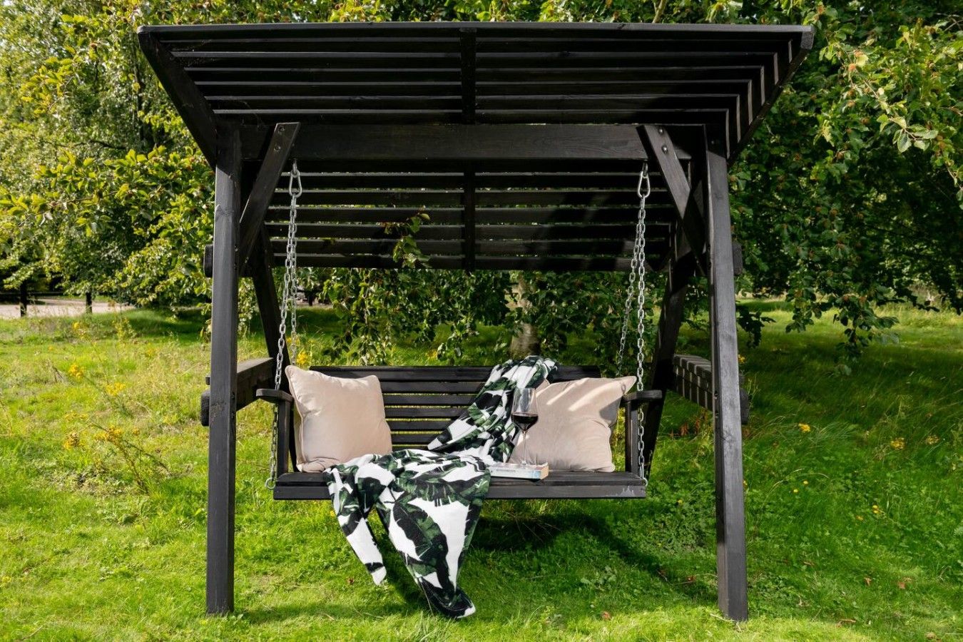 Una silla mecedora de madera con cojines, ubicada en un jardín con césped y árboles.