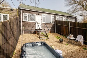 Un jardin avec un jacuzzi, une terrasse en bois, une petite table avec une chaise et une clôture en bois.