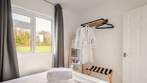 Una habitación de hotel con cama, un banco, una ventana y un perchero para bata.