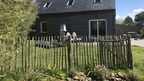 Ett tvåvåningshus med ett mörkt tak, en skorsten och ett trästaket framför.