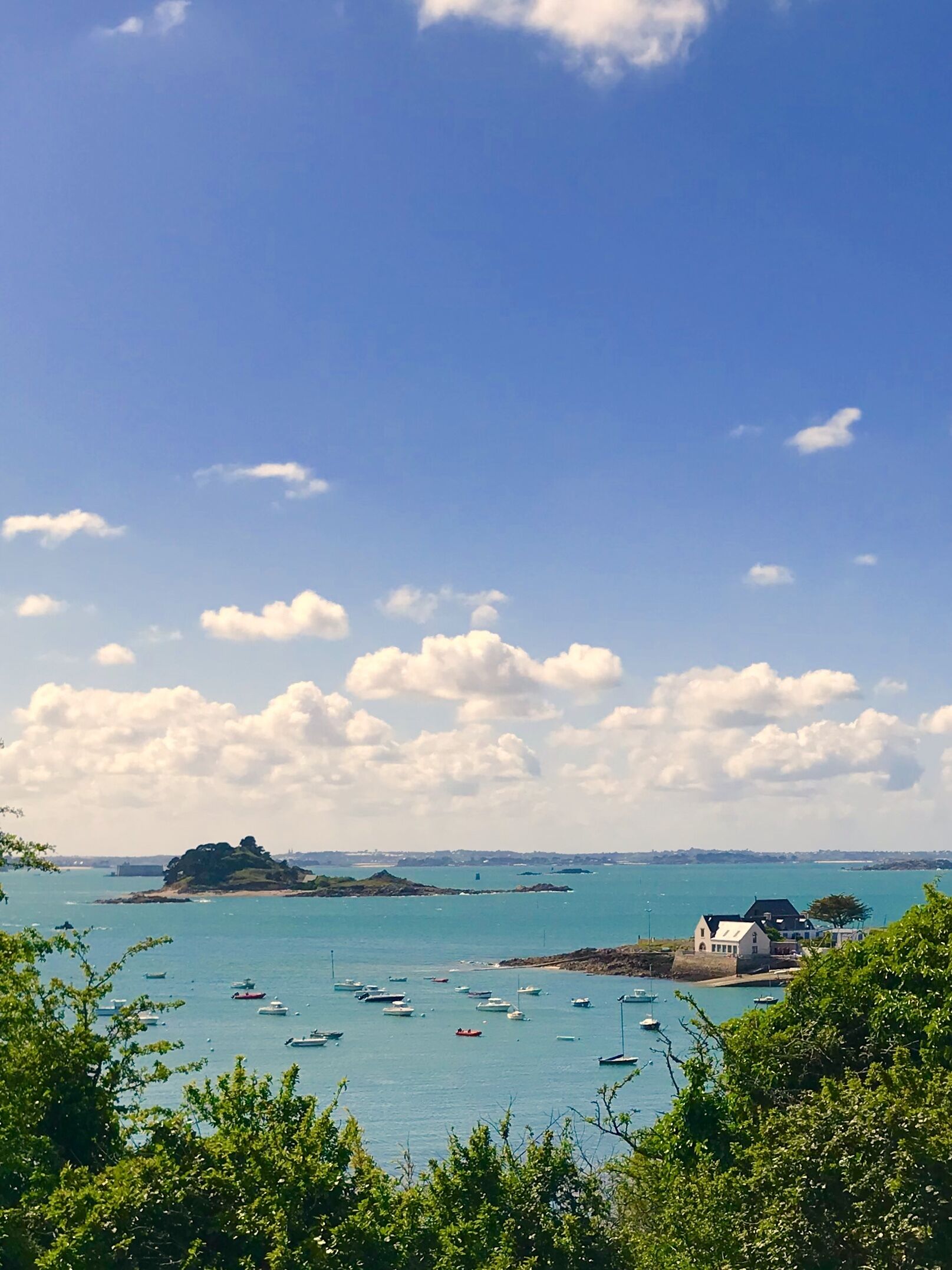 Vista costera con barcos, una pequeña isla y un edificio de fachada blanca.