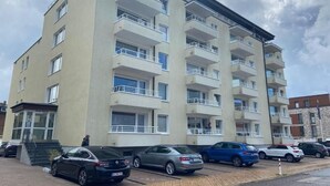 Un edificio residencial de varios pisos con balcones, un estacionamiento con varios coches y un cielo despejado.