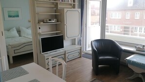 Una habitación con cama, televisión, escritorio con silla y ventana con vista a un edificio.