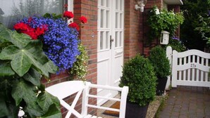 Une maison en briques avec une porte blanche, un banc blanc et des plantes en pot.
