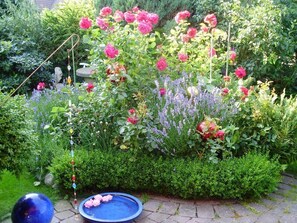 Um jardim com diversas flores, um comedouro para pássaros e um elemento decorativo azul com água.