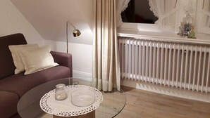 Un salon moderne avec un canapé, une table basse en verre, un radiateur et une fenêtre avec des rideaux.
