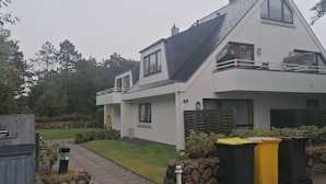 A modern two-story house with a sloped roof, a balcony, and a well-maintained lawn. - App. Neptun (Wenningstedt-Braderup)