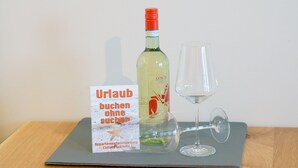 A bottle of Gosch wine and a glass on a table with a book titled "Urlaub buchen ohne suchen" by Christoph Schmitz. - Sylter Krebs, Haus Ankerlicht, Wohnung 65 (Sylt)