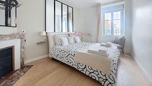 Un dormitorio con cama, chimenea, ventana con cortinas y vista a edificios.