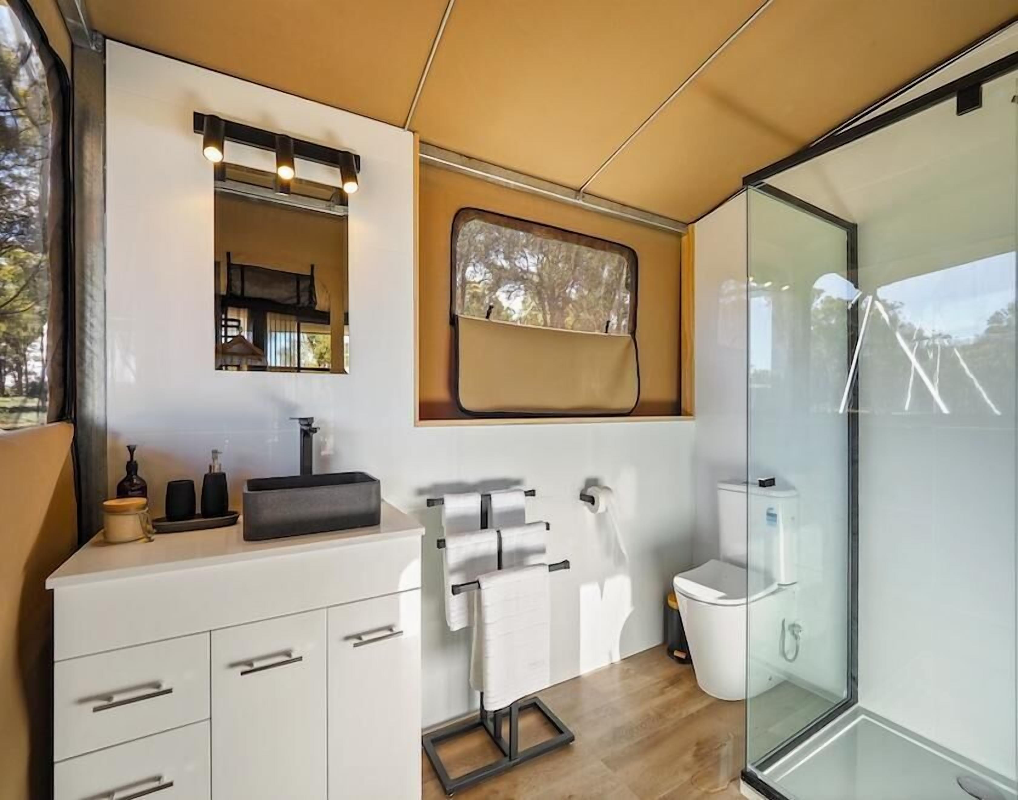 A modern bathroom with a white vanity, a mirror, a window, and a glass shower enclosure.