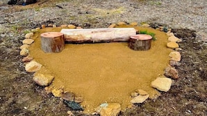 A circular fire pit with logs and stones arranged around it in a forest setting.