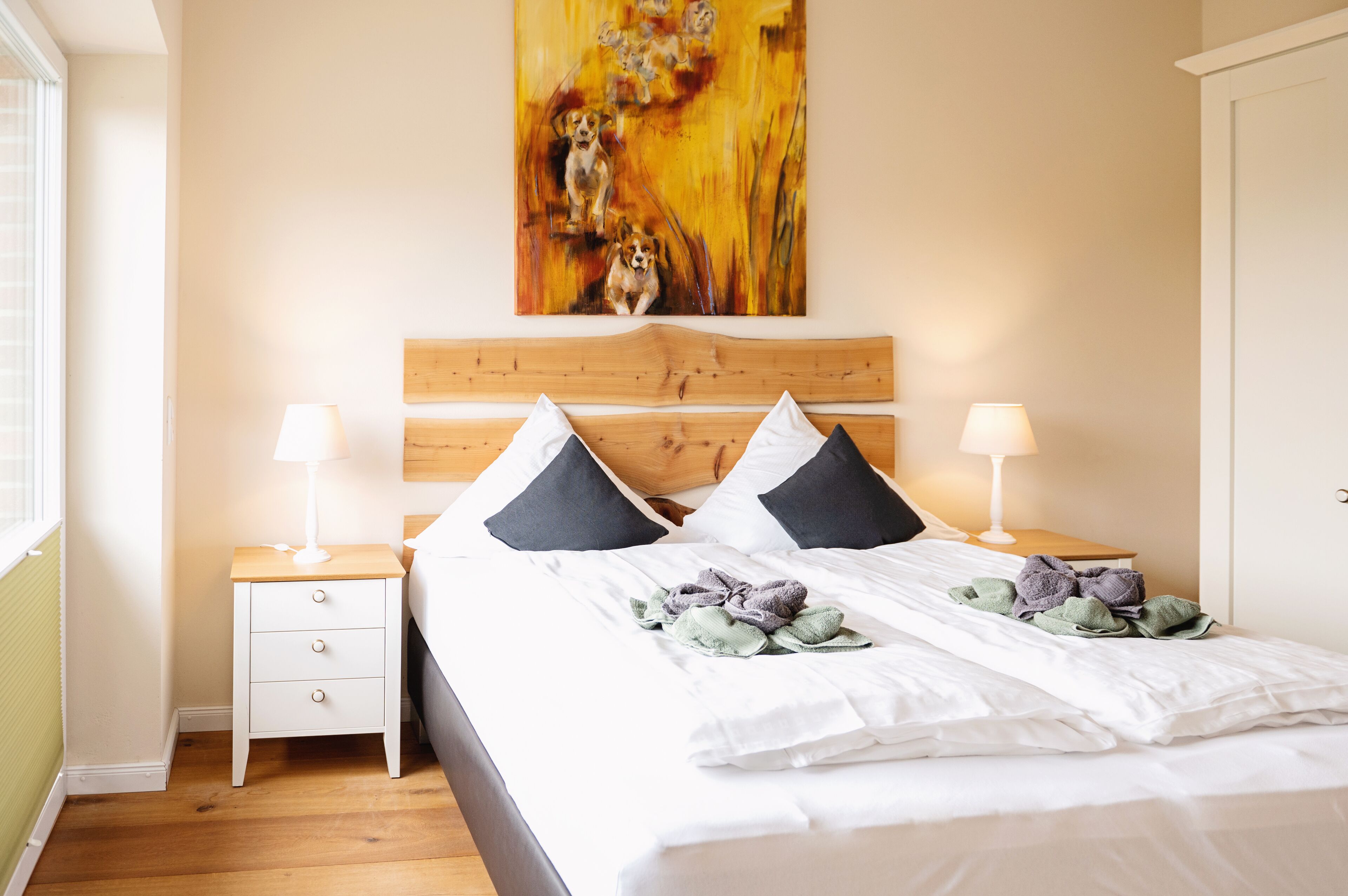 A neatly made bed with white linens, two black pillows, and a floral artwork above it.