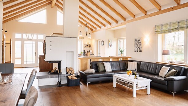 Un vaste espace de vie doté d’un plafond en bois, d’un canapé en cuir noir, d’une table basse blanche et d’une table à manger avec des chaises.