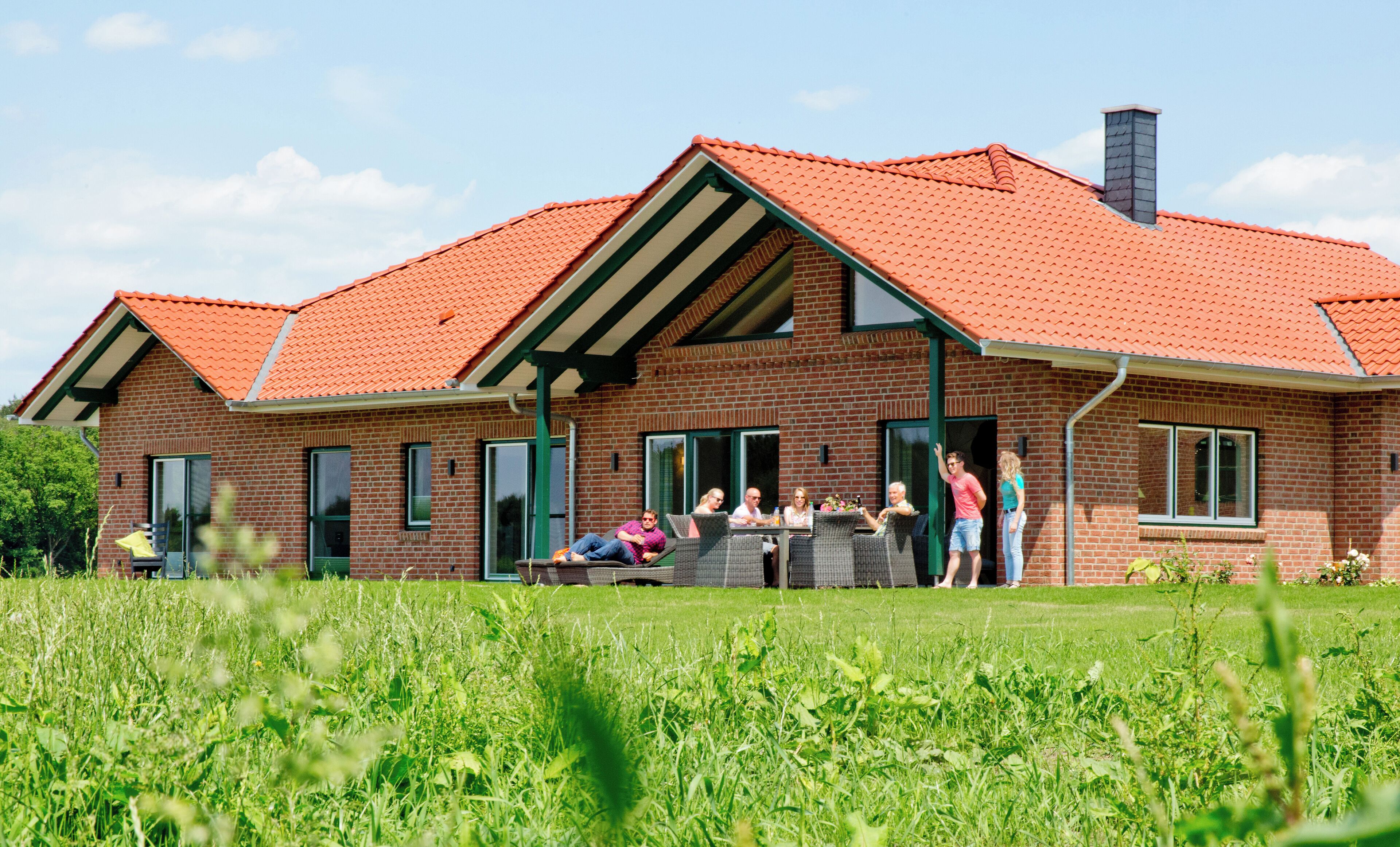 A two-story brick house with a red-tiled roof and green-framed windows.