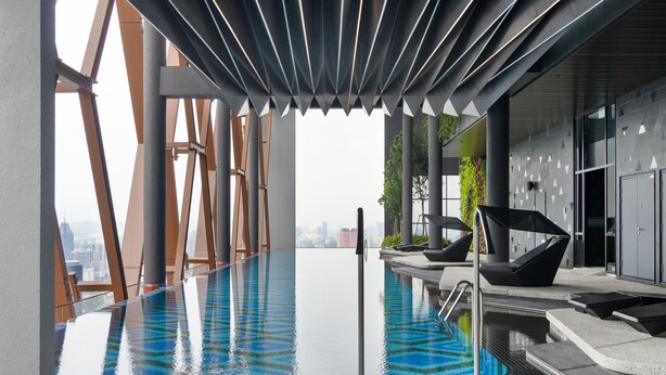 Une piscine intérieure moderne, dotée d’un plafond au design géométrique, de murs en verre transparent et offrant une vue sur le paysage urbain.