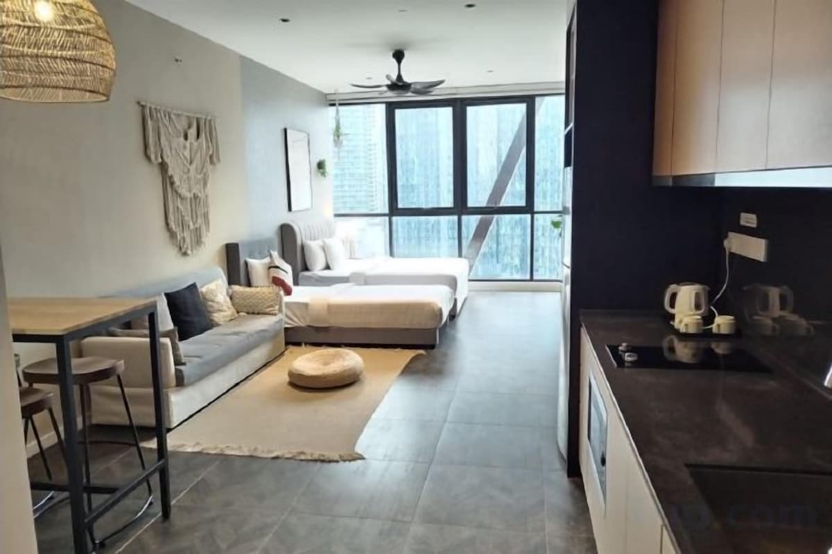 Un espace de vie moderne comprenant un canapé, un pouf et une table à manger, une cuisine équipée et de grandes fenêtres offrant une vue dégagée.