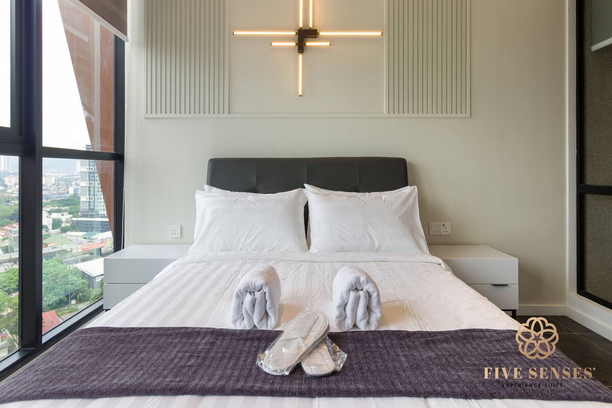 A modern hotel room with a large bed, white linens, a dark headboard, and a cross-shaped light fixture.