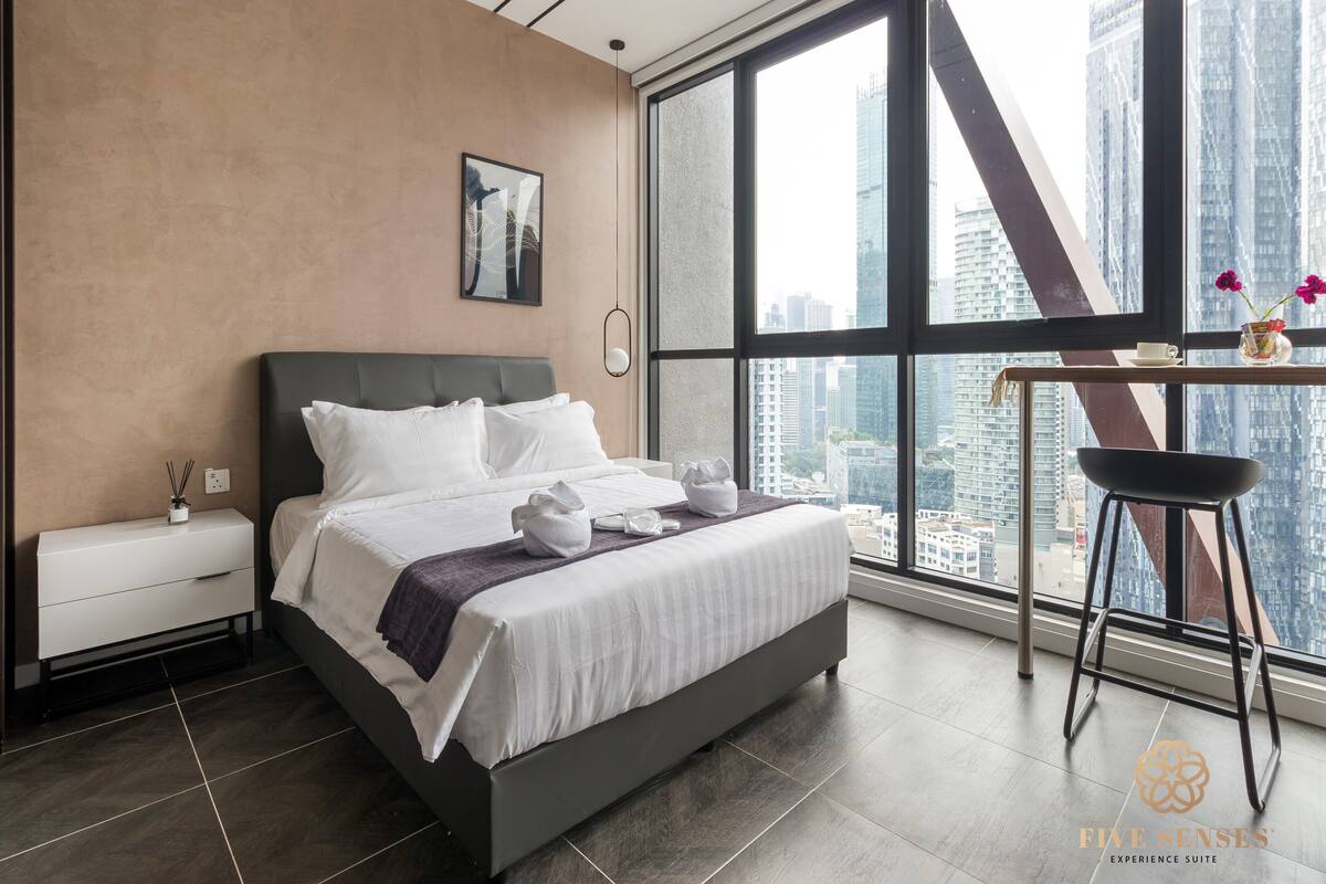 A modern hotel room with a large bed, a nightstand, a desk with a chair, and a large window offering a city view.