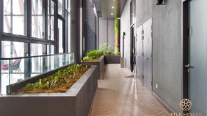 Un couloir moderne avec de grandes fenêtres, un bac à plantes orné de verdure et un motif de parquet en chevrons.