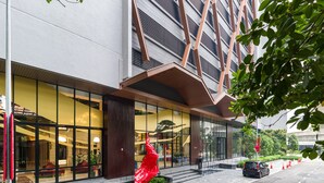 Un bâtiment moderne doté d’une façade en verre, d’une sculpture rouge et d’un espace paysager agrémenté d’un élément aquatique.