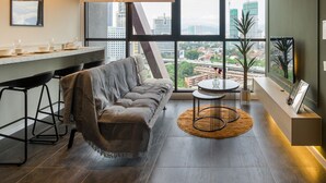 Un salon moderne avec un canapé, un coin repas doté d’un bar, une grande fenêtre offrant une vue sur la ville et un ventilateur de plafond.
