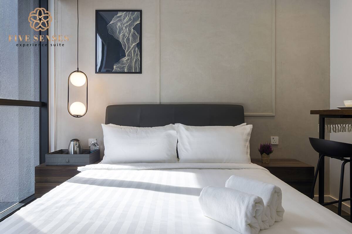A neatly made bed with white linens, a dark headboard, and a wall-mounted abstract artwork.