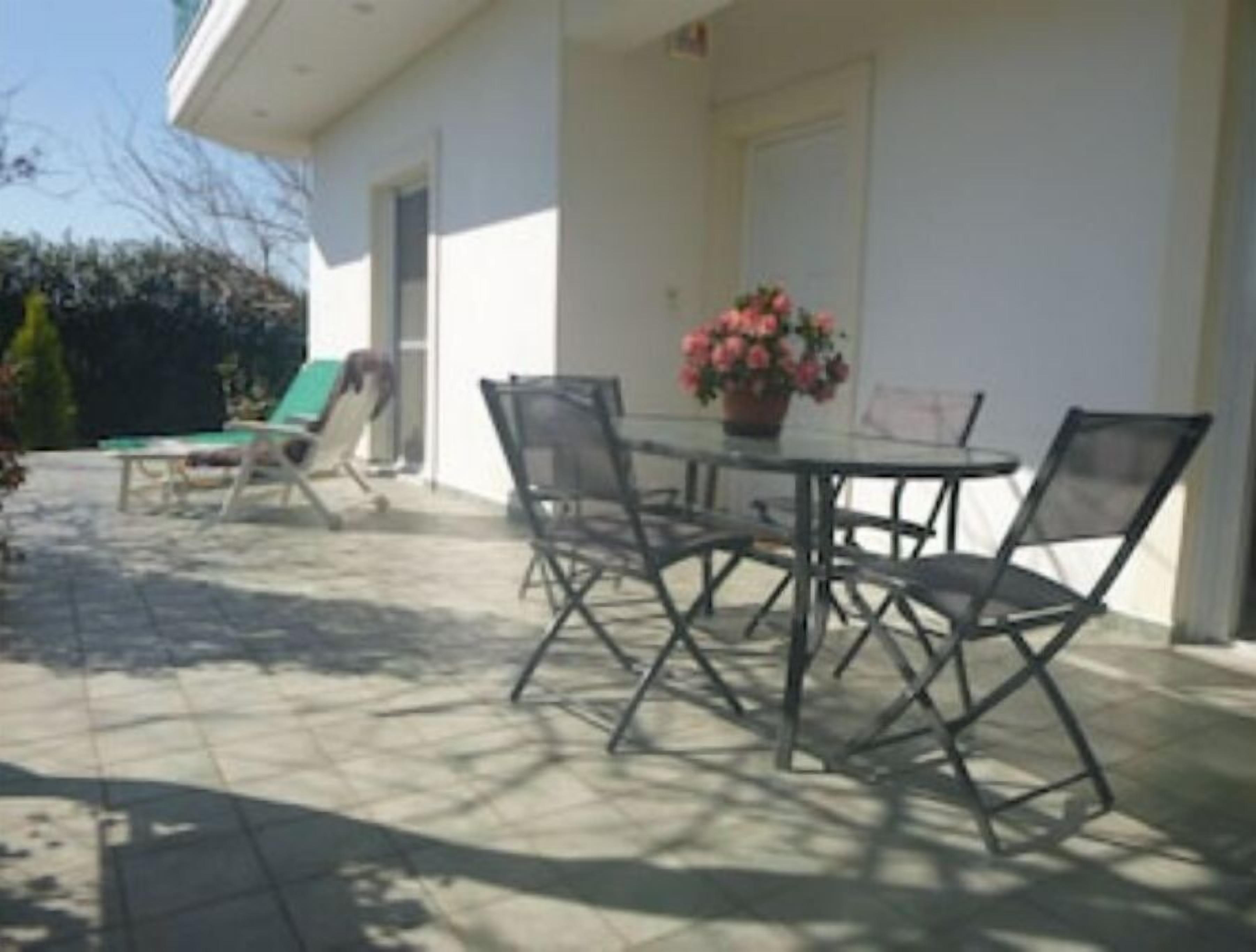 Une terrasse avec une table et des chaises, un pot de fleurs et une porte.