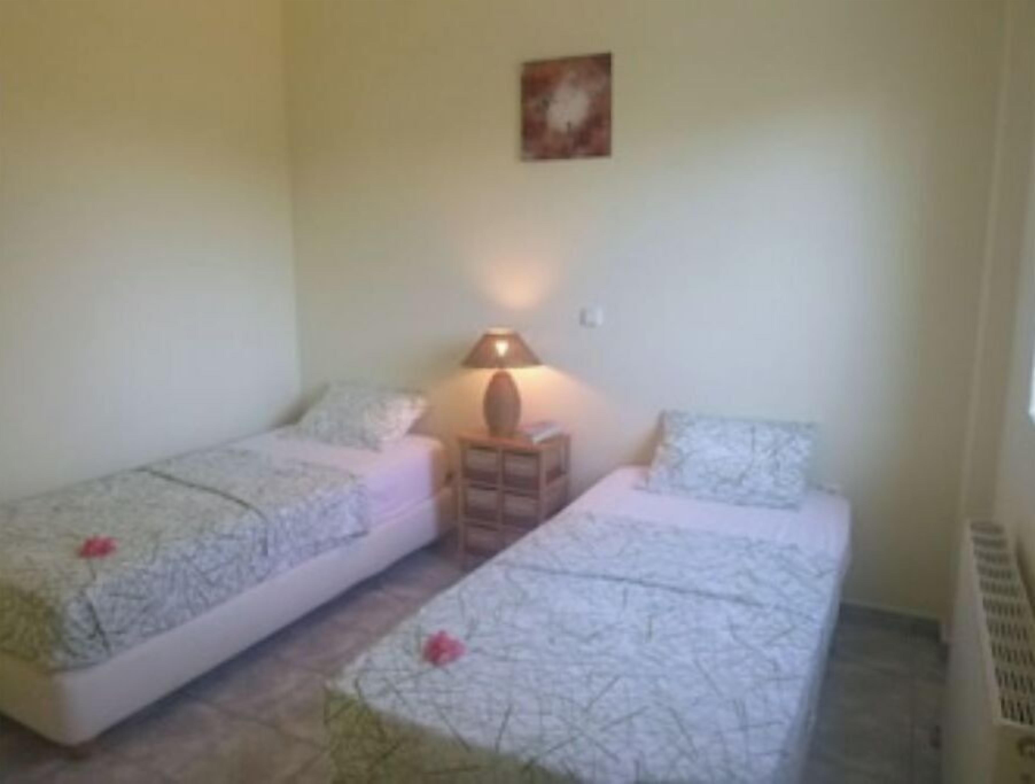 A small, clean room with two single beds, a nightstand with a lamp, and a wall-mounted picture.