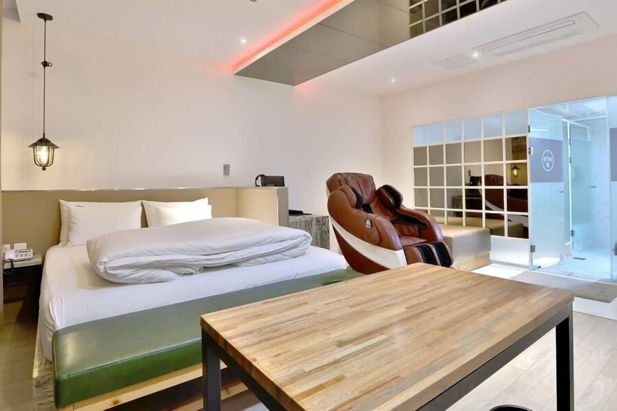 A modern hotel room with a bed, a massage chair, and a wooden table.