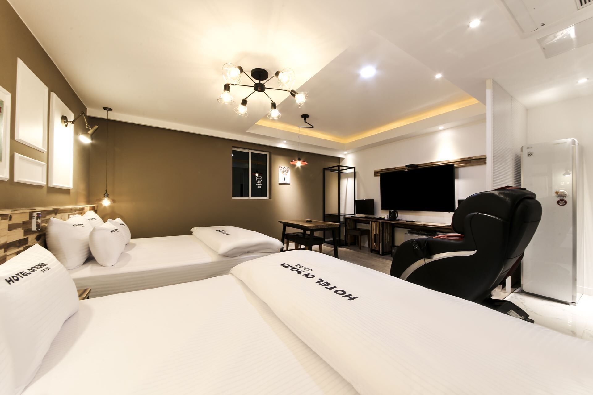 Ein Hotelzimmer mit zwei Betten, einem Schreibtisch, einem Sessel, einem Fernseher und einer Minibar.